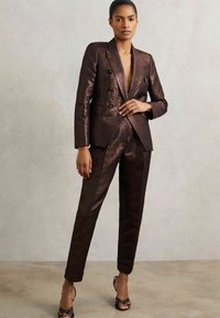 Brązowy metaliczny garnitur biznesowy z dopasowaną, dwurzędową marynarką z dużymi guzikami oraz slim-fit spodniami. Gładka tekstura i elegancki design.