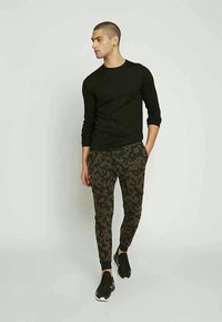Black long-sleeve shirt, green camouflage sweatpants with pockets, and black athletic shoes. Fitted design and tapered leg.