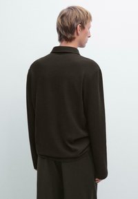 Camicia a maniche lunghe marrone scuro con colletto e tessuto testurizzato. La parte posteriore presenta una vestibilità comoda e un delicato dettaglio drappeggiato sull'orlo.