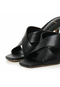 Sandali neri in pelle con design a cinturino incrociato. Stile open-toe e texture liscia, caratterizzati da un'estetica minimalista e tacco basso.