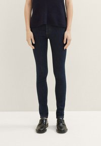 Jeans ajustados de mezclilla en un lavado oscuro, con una textura suave y un ajuste clásico, combinados con zapatos negros para un look elegante.