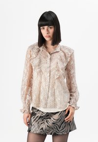 Genomskinlig, beige blus med volang fram och långa ärmar, prydd med små metalliska prickar. Stylar med en silverfärgad kjol med zebramönster.