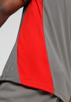 Primo piano di una persona che indossa una maglietta grigia con un pannello laterale rosso acceso e pantaloni grigi abbinati.