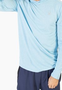 Light blue long-sleeve hoodie with a textured pattern, featuring a hood and a subtle logo, paired with dark navy pants.