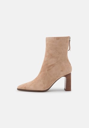 Beige rågummistøvle med spids tå, stablet træblokhæl og lynlås bagpå.