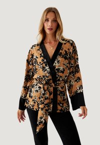 Blusa envolvente floral en un tono marrón cálido con patrón floral negro. Presenta un profundo escote en V, mangas largas y un cinturón atado en la cintura. Textura de tela suave.