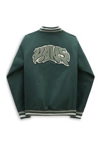Tummanvihreä yliopistojakku, jossa on raidalliset hihansuut ja kaulus. Takana on suuri tekstuurinen "VANS"-logotypografia tyylitellyssä fontissa.