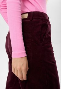 Burgundy kordfluga byxor med sidfickor och en ljusbeige etikett på midjan. Tillsammans med en figurnära rosa ribbad långärmad topp.