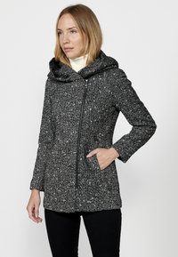 Kapucňová bunda v čierno-bielej textúrovanej látke, s predným zipsom, bočnými vreckami a útulnou prehýbajúcou sa kapucňou.