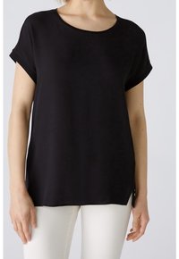 Top nero a maniche corte con scollatura rotonda, texture morbida e rifiniture arrotolate, dotato di spacco laterale per un fitting rilassato.