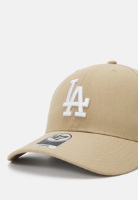 Beige baseball caps med en hvit brodert "LA" logo på forsiden. Har en buet skjerm og en 47-merket tagg på siden.