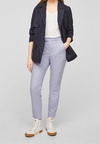 Granatowy, dwurzędowy płaszcz trench nad biały t-shirt, lawendowe spodnie i białe trampki z wysoką cholewką i gumową podeszwą. Gładka faktura materiału.