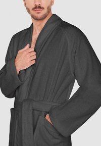 Bata de baño gris oscuro hecha de una tela suave. Presenta un cuello de chal, mangas largas, bolsillos laterales y un cinturón a la altura de la cintura.
