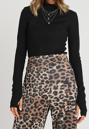 Donna che indossa un dolcevita nero a maniche lunghe e pantaloni a vita alta con stampa leopardata, con collane d'oro sovrapposte.