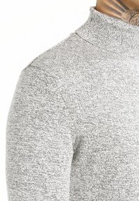 Pull gris en tricot avec un col montant, un tissu texturé et une coupe ajustée autour du cou et des épaules. Matière douce.