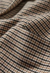 Ruskea ja musta houndstooth-kankaan pehmeällä tekstuurilla, jossa on kudottu kuvio kermaisella taustalla, esittelee syvyyttä ja liikettä.