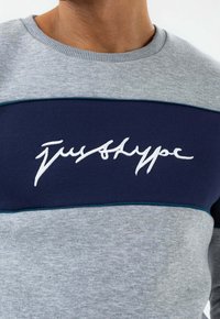 Szary sweatshirt z granatowym poziomym panelem, haftowanym białym napisem "justhype" na środku oraz detalami przy okrągłym dekolcie w prążki.