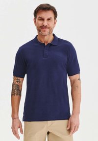 Granatowa koszulka polo z miękkiego materiału, z krótkimi rękawami, klasycznym kołnierzykiem i dwoma guzikami. Posiada subtelne logo.