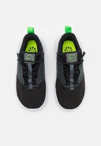 Black athletic shoes with mesh upper, green accents, and a white speckled sole. Features a pull tab and lace-less design for easy wear.