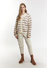 Cardigan a righe in crema e marrone, con bottoni sul davanti, vestibilità oversize, abbinato a pantaloni beige chiaro e stivali alla caviglia marroni, texture liscia.