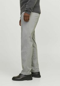 Helle graue Baumwollhose mit Slim Fit, ausgestattet mit Seitentaschen, glatter Textur und kombiniert mit schwarzen Schuhen.
