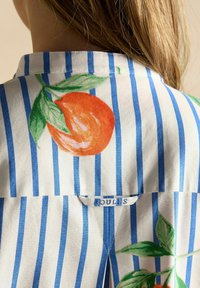 Weißes Stoffhemd mit blauen Streifen, mit einem großen orangefarbenen und grünen Blätterdesign auf der Rückseite, Etikett mit der Aufschrift "BOULDS".