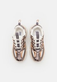 Lace-up sneakers with metallic bronze and silver panels, beige outsole, and white mesh detailing. Features padded collar and pull tab.