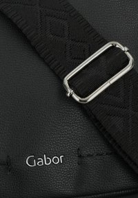 Bolso de mano de cuero negro con un acabado texturizado, que presenta una correa tejida negra y una hebilla de metal plateado. Logo de Gabor en plata adjunto.