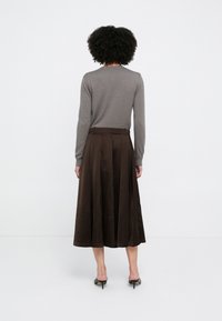 Gonna plissettata marrone con vita alta, realizzata in materiale liscio, abbinata a una maglia grigia aderente a maniche lunghe e mule nere con tacco.