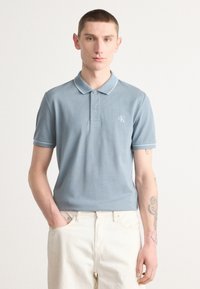 Lyseblå polo skjorte laget av bomull, med klassisk krage, to-knappings placket og subtil kontrastkant. CK-logo brodert på brystet.
