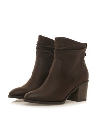 Botas de cuero marrón hasta el tobillo con un diseño holgado, punta afilada y tacón apilado. Presentan un sutil acento lateral cerca del tacón.