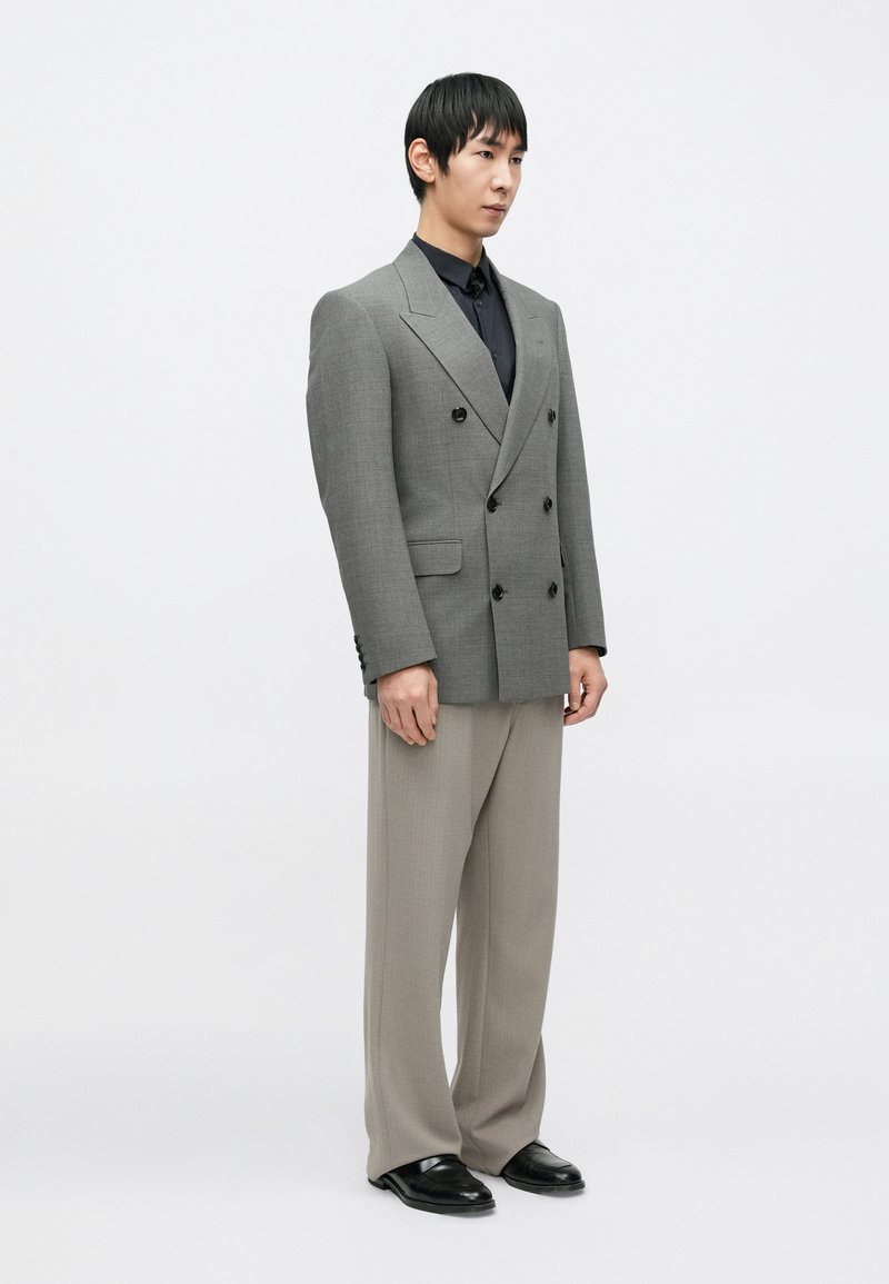 Gray double-breasted suit jacket, black shirt underneath, light gray trousers, black shoes, structured fit, smooth texture, minimalistic design.