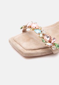 Beige Wildledersandale mit quadratischer Spitze und einem mit bunten Edelsteinen in verschiedenen Formen und Größen besetzten Riemen.