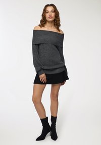 Sweter w kolorze ciemnoszarym, odsłaniający ramiona, z prążkowanym dekoltem, zestawiony z czarną mini spódnicą i czarnymi botkami za kostkę. Gładki materiał i dopasowany krój.