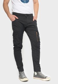 Zwarte cargobroek met slim fit, voorzien van zijzakken, een voorzak met rits, en een denim-achtige textuur, gecombineerd met grijze high-top sneakers.