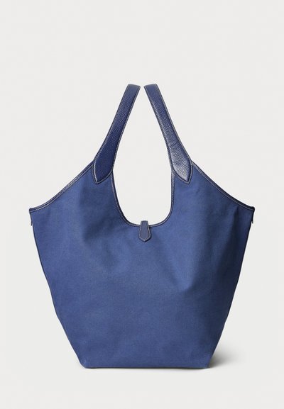 Blå tygväska med texturerad yta och släta läderdetaljer. Har breda remmar och en rymlig design med en minimalistisk look.