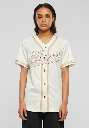 Kurze Baseball-Trikotärmel in Creme mit vertikalen Nadelstreifen, mit beigen Akzenten, schwarzen Knopfverschluss und einem gestickten Logo auf der Vorderseite.