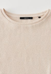 Maglione lavorato a coste in beige con scollo a girocollo. Presenta una leggera texture e un'etichetta con la scritta "someday" sul colletto.