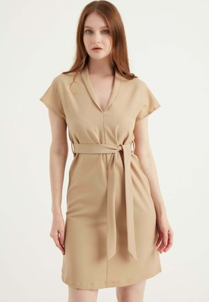 Beige jurk van gladde stof, met een V-hals, korte mouwen en een taille met een bijpassende riem. Eenvoudig, aansluitend ontwerp.