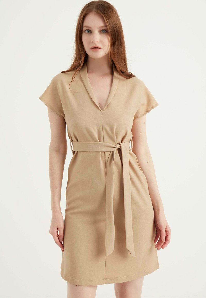 Beige jurk van gladde stof, met een V-hals, korte mouwen en een taille met een bijpassende riem. Eenvoudig, aansluitend ontwerp.