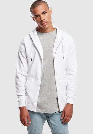Hvid zip-up hættetrøje med snoretræk, to frontlommer, båret over en grå t-shirt, kombineret med lysblå jeans. Glat tekstur, minimalistisk design.