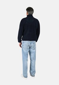 Maglione in pile blu navy con colletto alto e finitura testurizzata, abbinato a jeans a gamba dritta celeste e sneakers bianche.