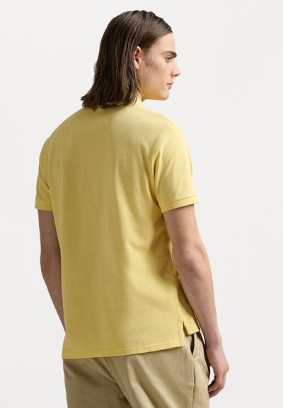 Tricou polo de culoare galben deschis, cu mâneci scurte, fabrică texturată, fante laterale la tiv, guler clasic, croi lejer.