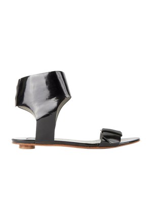Sandale plate en cuir verni noir avec bride à la cheville et petit talon bloc, bout ouvert et style minimaliste.