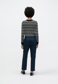 Ριγέ μαύρο και λευκό πουλόβερ με μακριά μανίκια, σε συνδυασμό με σκούρο μπλε παντελόνι. Η εμφάνιση διαθέτει κανονική εφαρμογή και κλασική σιλουέτα.