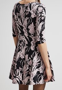 Svart klänning med trekvartslånga ärmar, med ett rosa blommönster. Passformen är utsvängd vid midjan, med en klassisk rund halsringning.