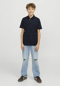 Marinblå polotröja med korta ärmar, kombinerad med ljusblå trasiga jeans och mörka sneakers med vita detaljer. Enkla, avslappnade kläder.