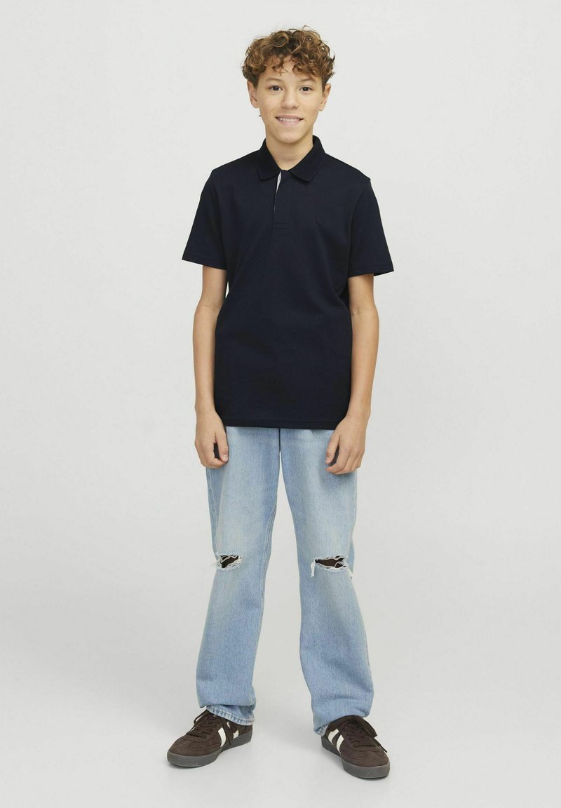 Marinblå polotröja med korta ärmar, kombinerad med ljusblå trasiga jeans och mörka sneakers med vita detaljer. Enkla, avslappnade kläder.