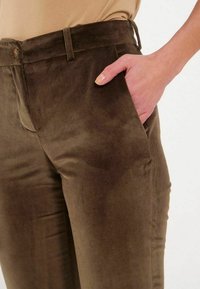 Pantalon en tissu brun, doux, ressemblant à du daim, avec une coupe ajustée, des poches avant et une fermeture simple à bouton et à glissière.