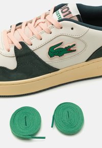 Lacoste sneakers with a white leather upper, green suede accents, pink laces, and a green embroidered logo. Includes green laces.
